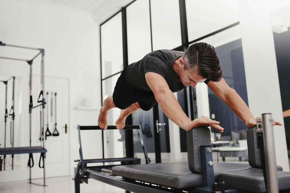 Hombre joven haciendo estiramiento en equilibrio sobre cama de pilates